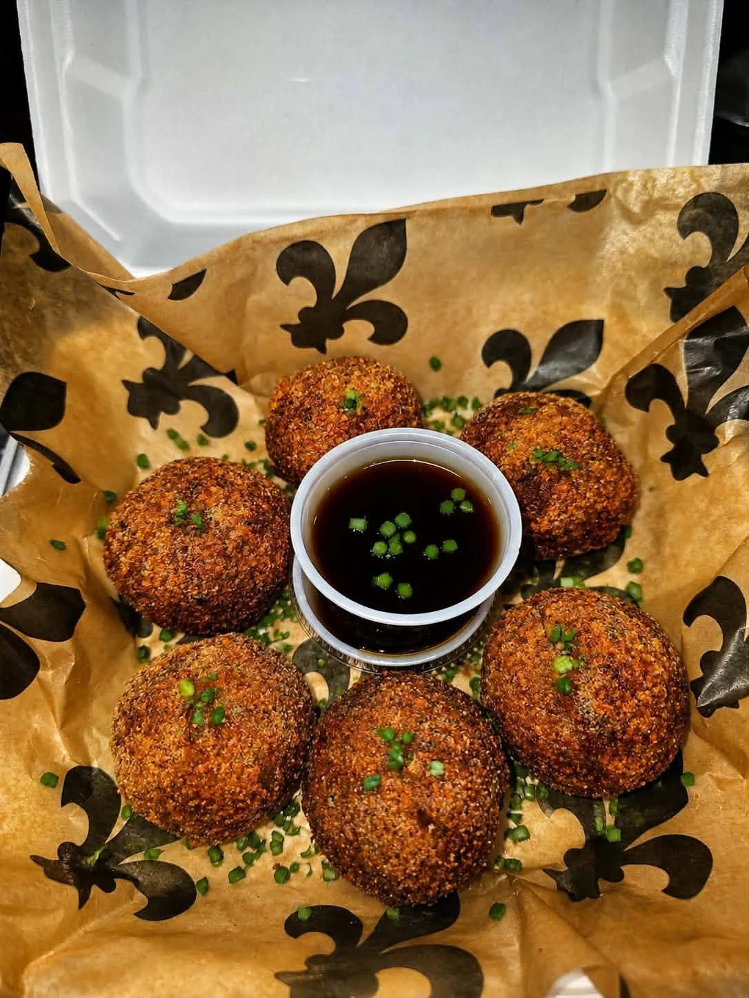 Six golden boudin balls arranged around a cup of dipping sauce.
