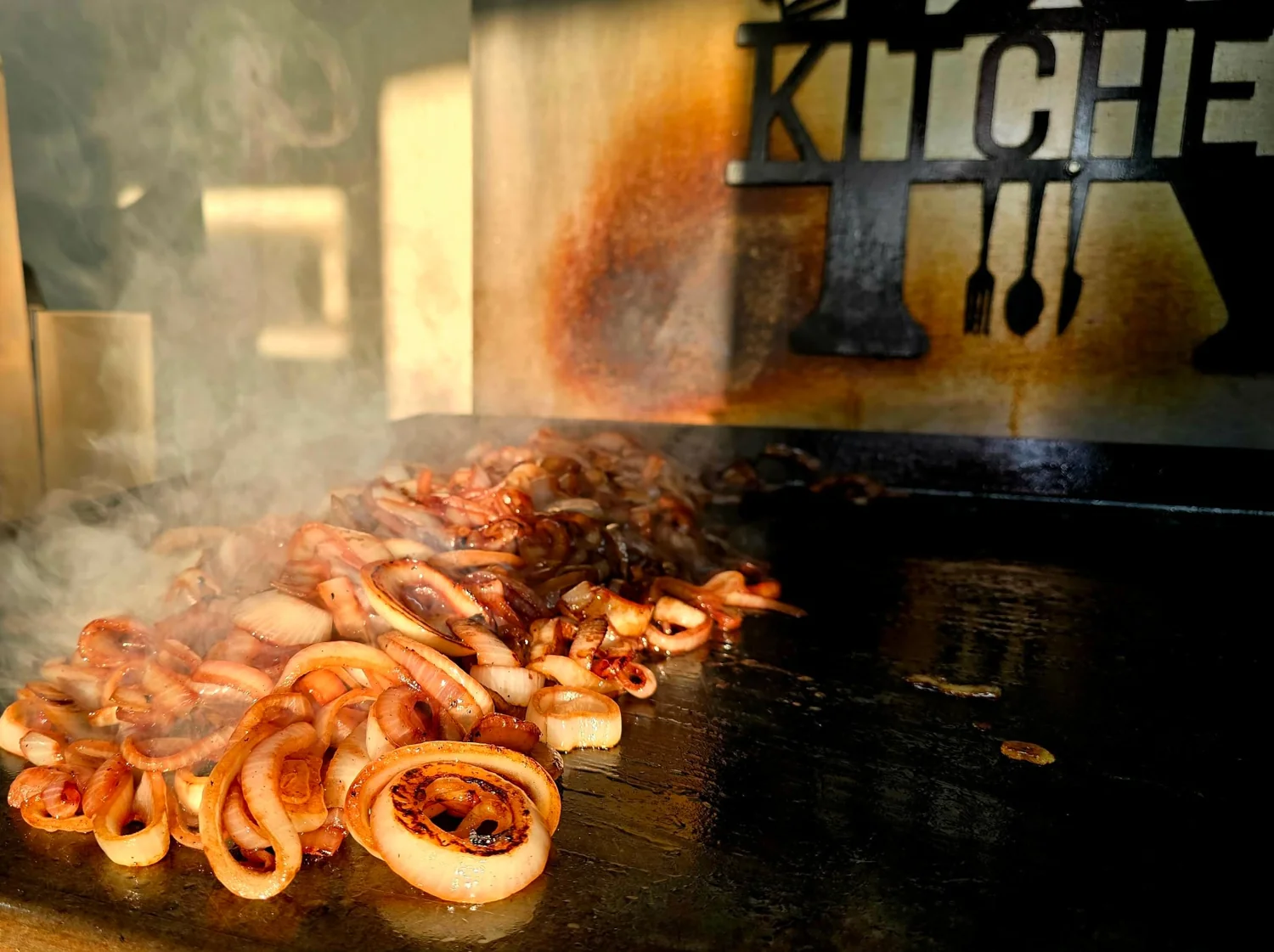 Sliced onions cooking on a steaming griddle.