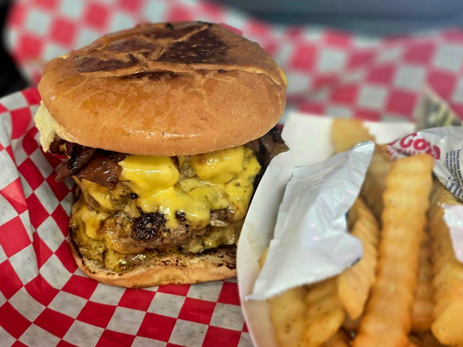 A double smash burger with melted cheese and grilled onions, served with fries.